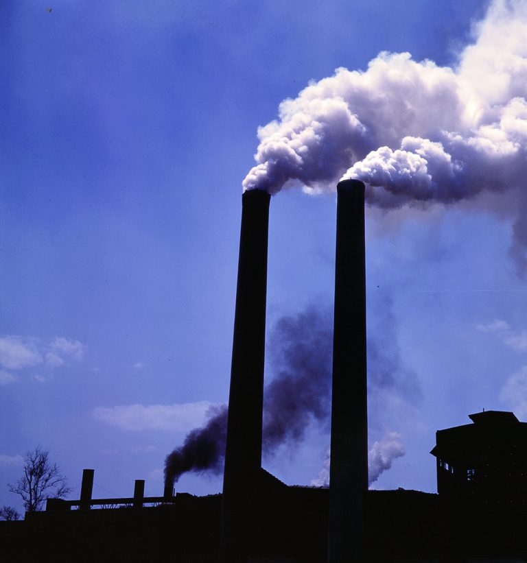 Två fabriksskorstenar som det kommer vit rök ur, mot en dunkle himmel. Foto: iStock