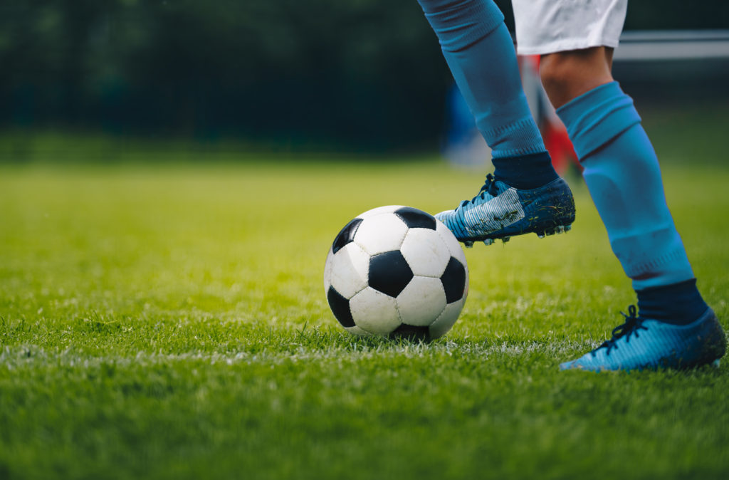 Blåklädda ben och fötter som är på väg att sparka en fotboll, mot grönt gräs.
