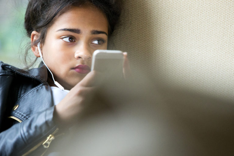 Ung flicka med hörlurar i öronen och en mobiltelefon, ser orolig ut. Foto: iStock