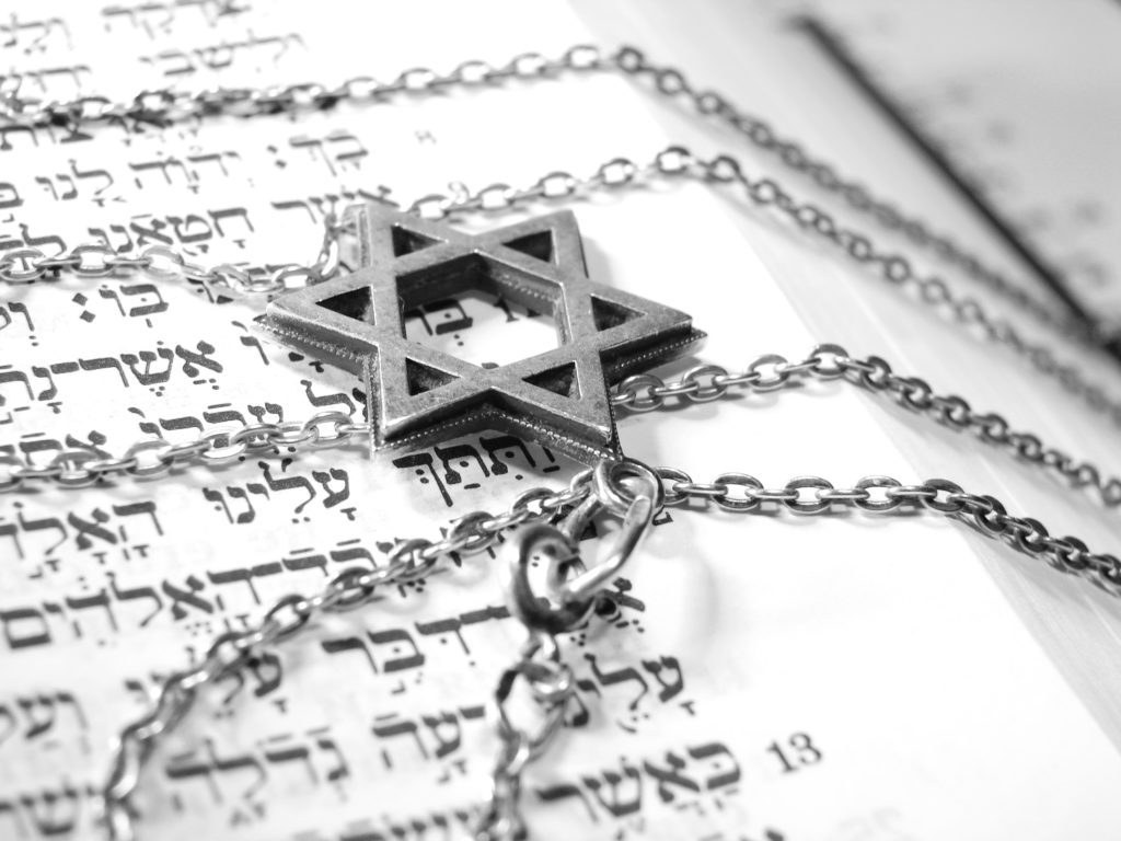 Bild på ett smycke föreställande en Davidsstjärna som ligger på en uppslagen sida med hebreisk text.