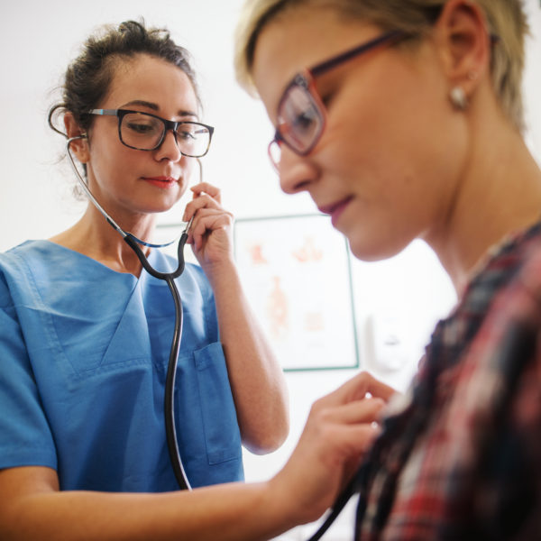 Kvinnlig läkare i blå sjukhuskläder undersöker en patient med stetoskop. Foto: iStock