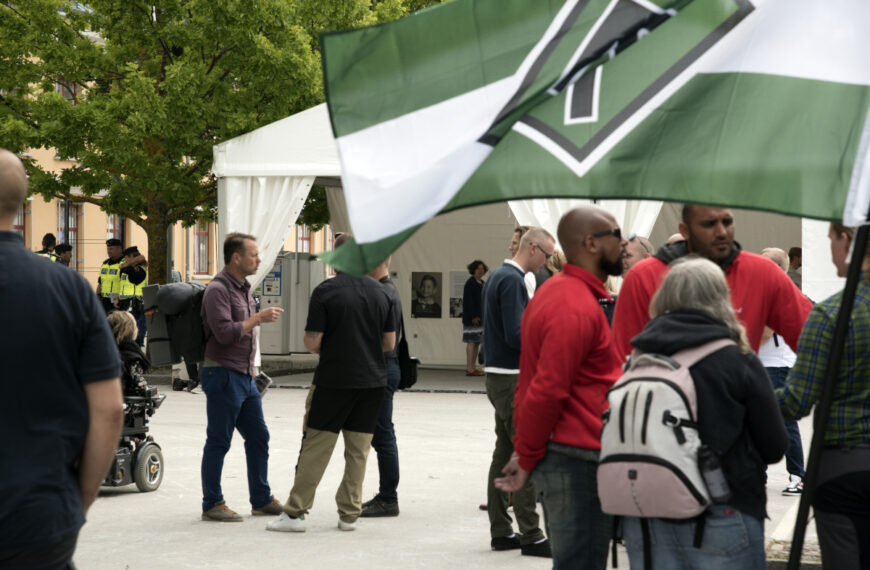 Bilden visar Nordiska Motståndsrörelsens tält i Almedalen, 2017. NMR:s flagga i förgrunden, Personer står runt omkring och diskuterar. En grupp poliser srtår i bakgrunden. Foto: Mattias Glassel, NU